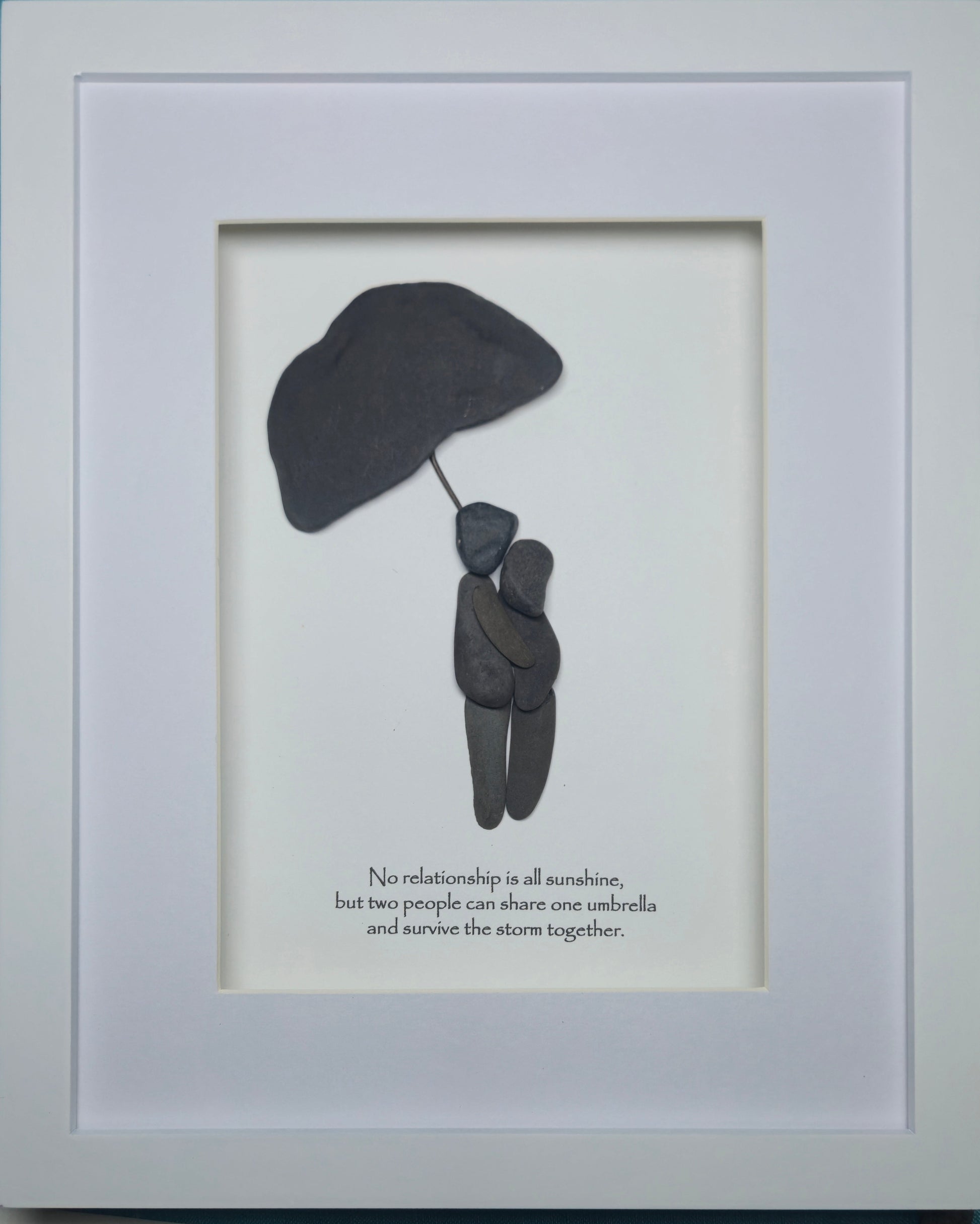 Framed wall art featuring a minimalist black silhouette of two people sharing one umbrella on a white background, with the quote 'No relationship is all sunshine, but two people can share one umbrella and survive the storm together.' printed below.