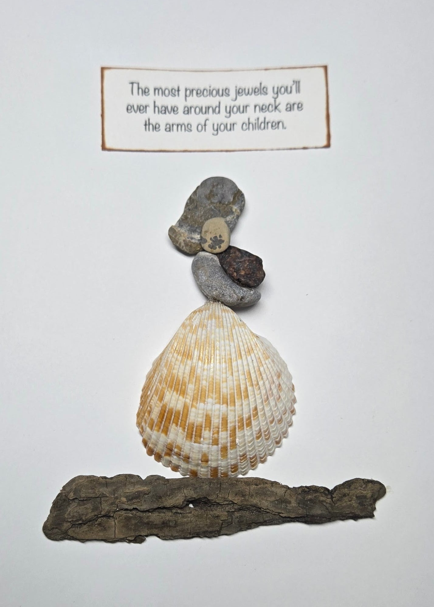 A decorative wall art piece featuring a mother and child arranged l on a piece of driftwood, with a small rectangular sign above reading, 'The most precious jewels you'll ever have around your neck are the arms of your children.'.